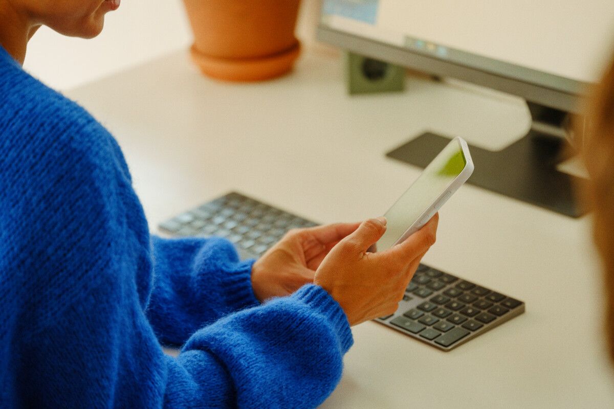 Dame som ser på mobilen mens hun sitter foran PC