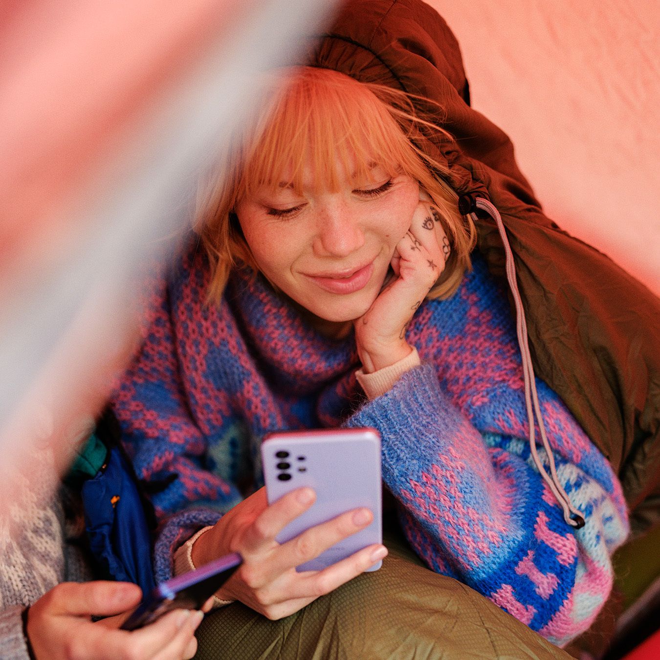 Ung kvinne i telt leser på mobilen og har mobilabonnement for unge