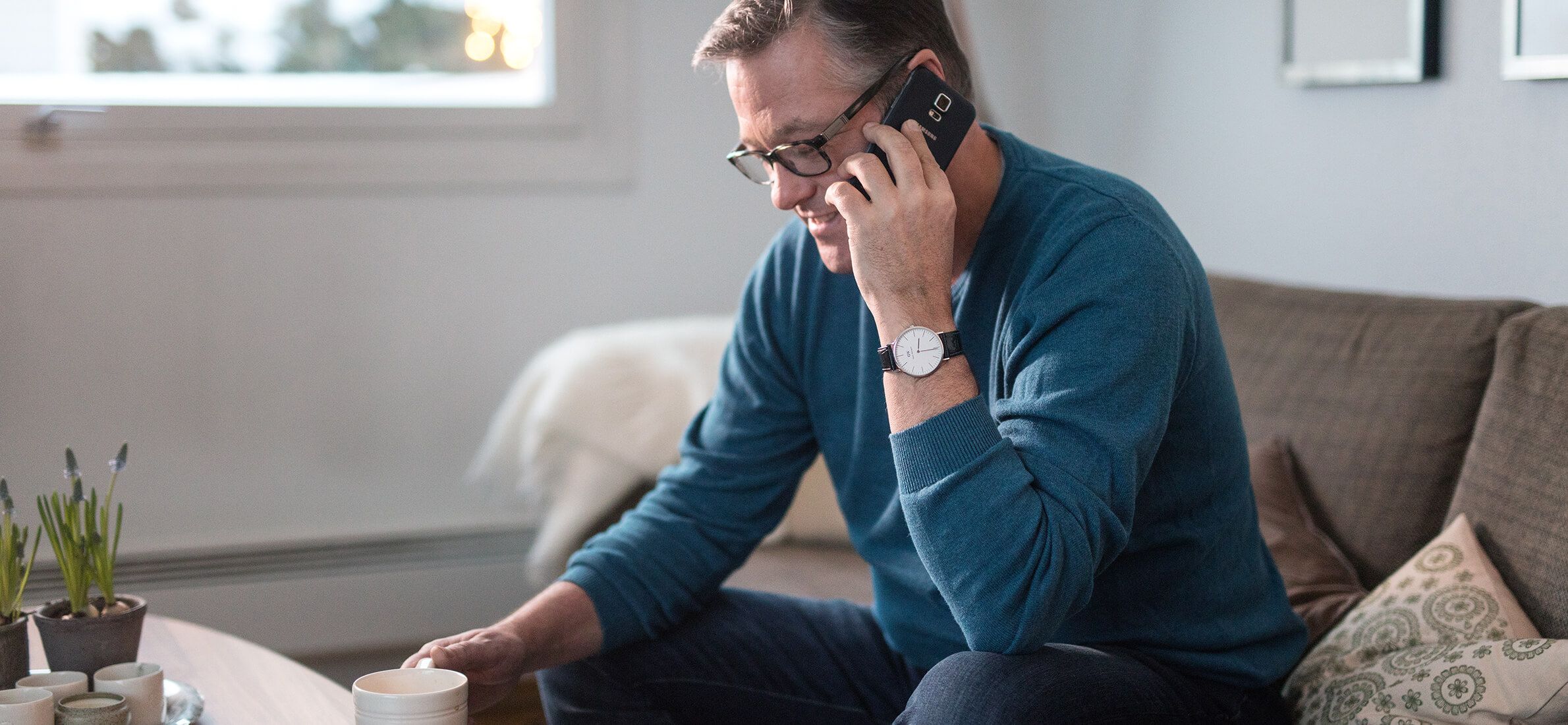 Mann sitter i sofaen og snakker i mobiltelefon