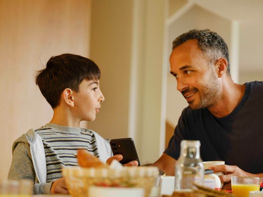 Sønn og pappa med mobil ved frokostbordet