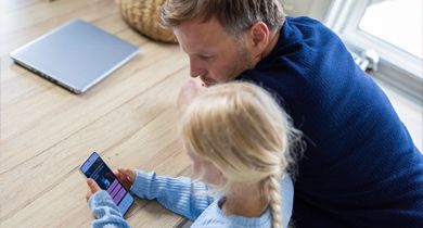 Far ser på mobiltelefon med sin datter