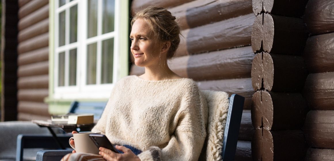 Kvinne som sitter med en kaffekopp i hytteveggen som er varmet opp på forhånd ved hjelp av M2M