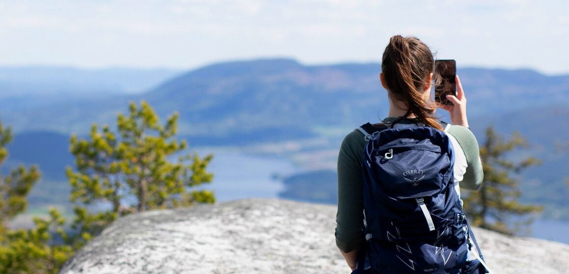 Kvinne med ryggsekk tar bilde av naturskjønn utsikt