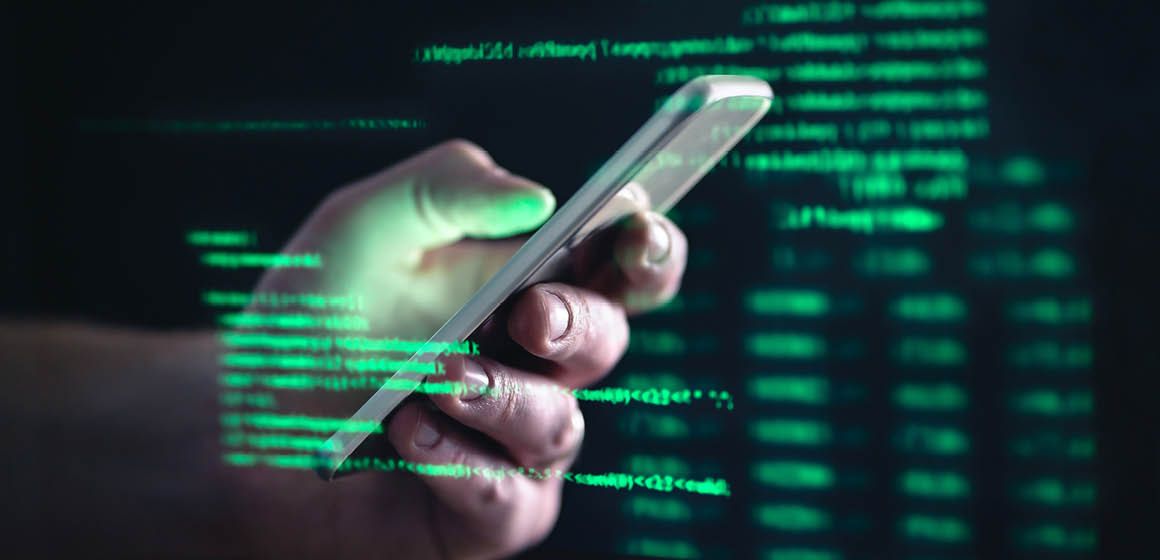 Hånd holder en mobiltelefon med grønn digital tekst i bakgrunnen