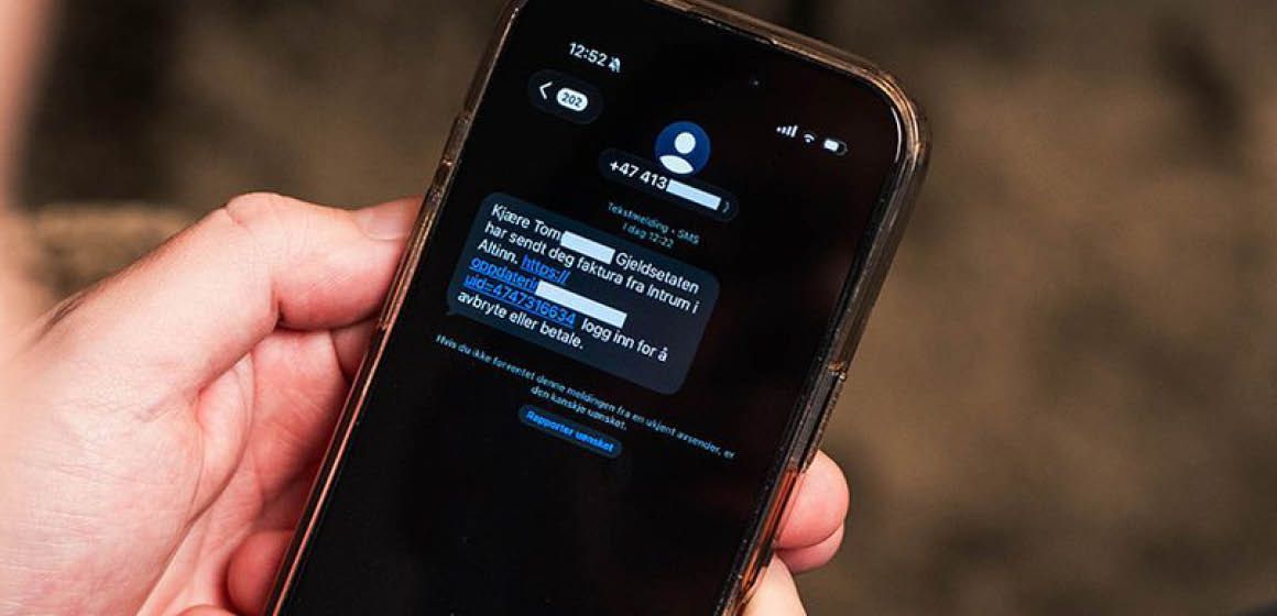 Hånd som holder en mobiltelefon med en SMS om en faktura fra "Gjeldsetaten"