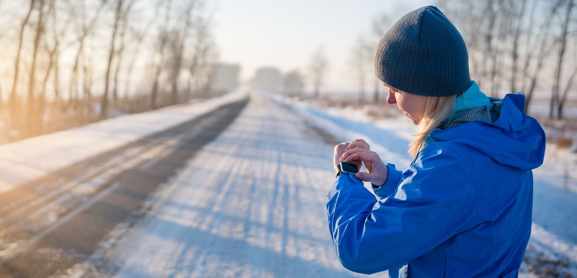 kvinne sjekker smartklokken på snøfylt vei om vinteren