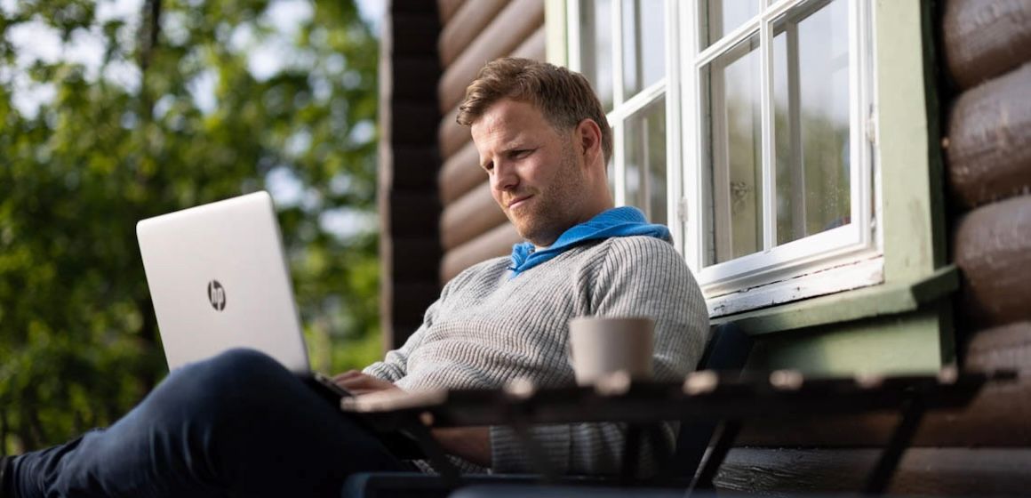 Trådløst Bredbånd på hytta: Mann i grå genser sitter ute på hytta og surfer på en PC.