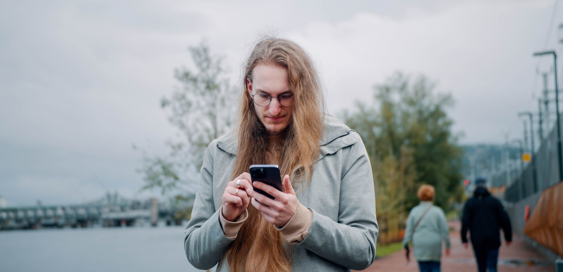 mann går utendørs og ser på mobilen sin