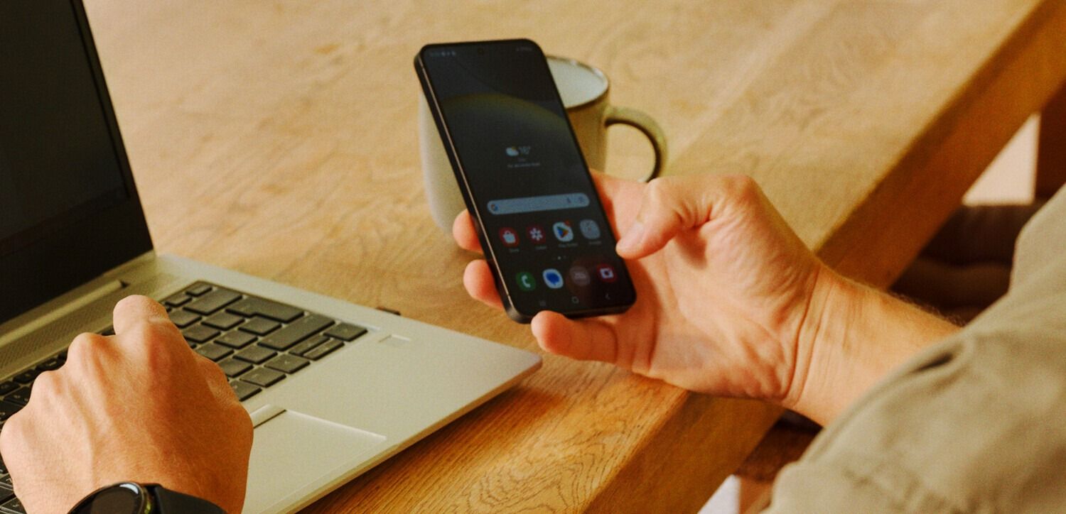 Person bruker bærbar PC og mobil ved bordet