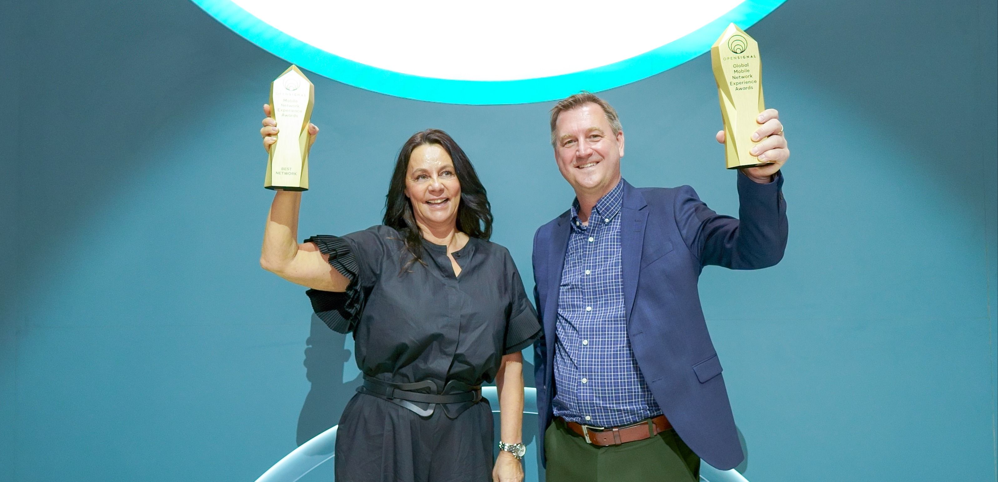 To personer holder priser opp foran en blå bakgrunn