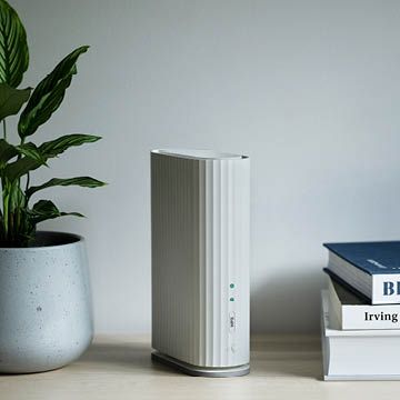 Moderne trådløs ruter på bord ved siden av plante og bøker