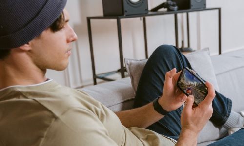 Mann sitter i sofaen og gamer på mobilen med 5G.