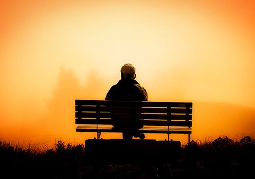 Eldre mann sitter på en benk og ser på solnedgang