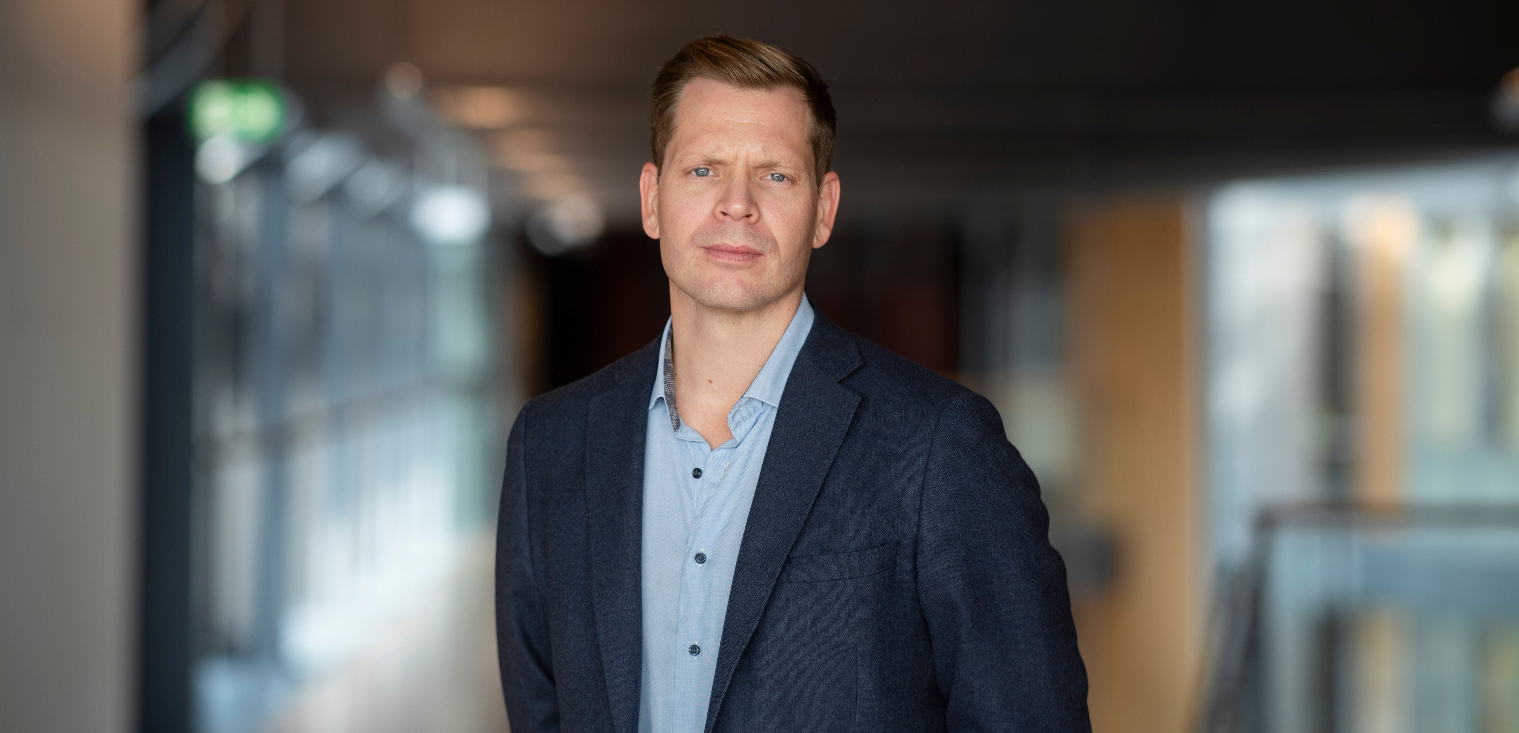 Mann i blå dressjakke og skjorte i lys kontorbygning