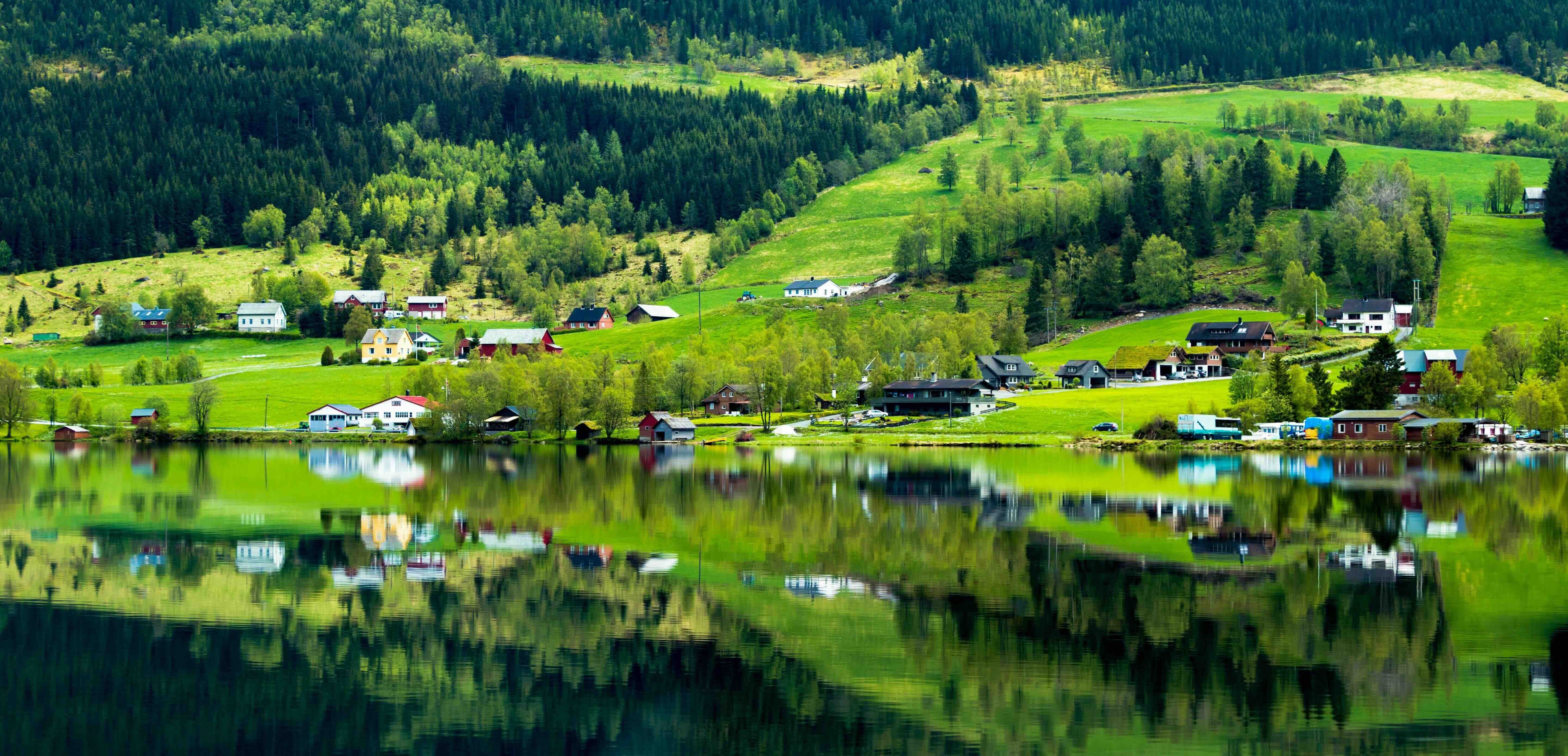 Idyllisk norsk landsby med hus og skog speilet i vannet