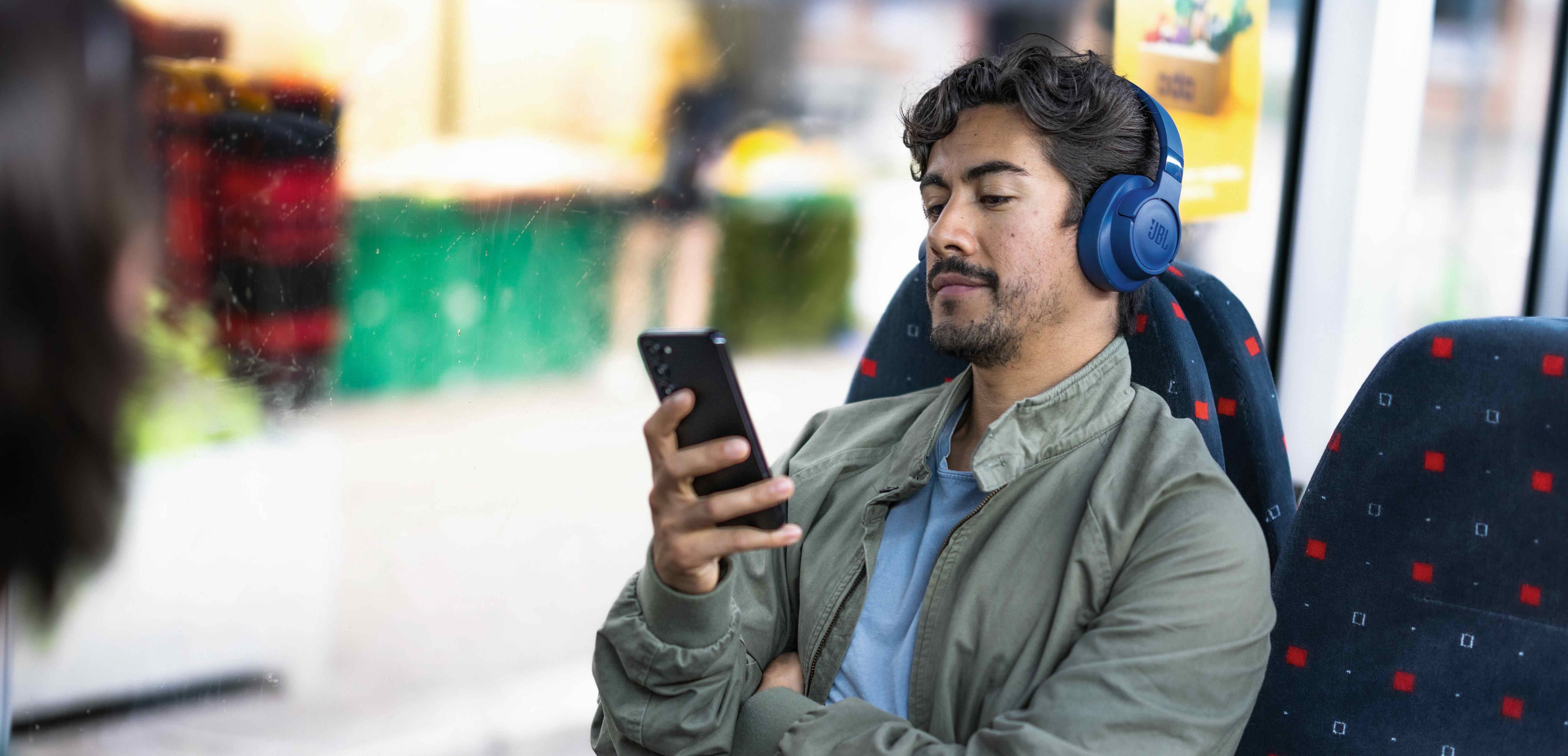 Person med hodetelefoner ser på mobil i buss