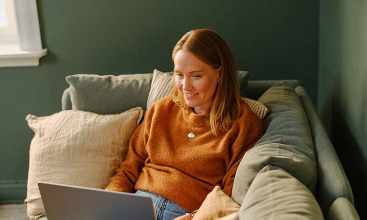 Kvinne med PC i sofa – med digital trygghet fra Telenor