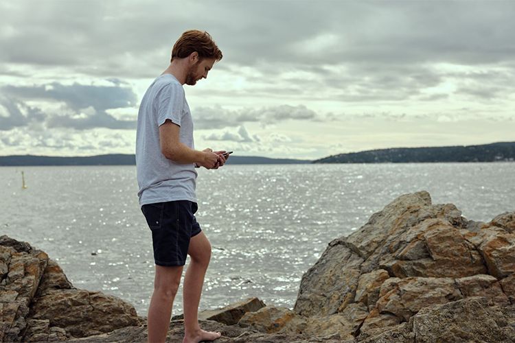 Mann på svaberg med mobil i hånden