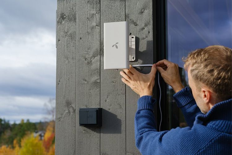 Mann skrur opp antenne på hytta for å få internett