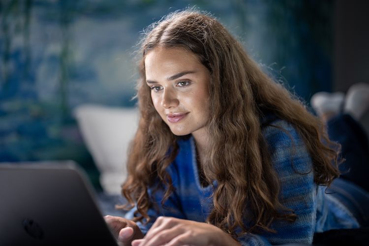 Dame som ligger på en seng med laptop og surfer på tryggere internett hjemme